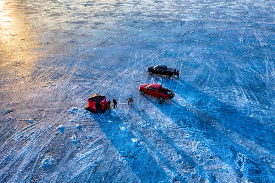 Drone shot of ice fishing scene with tents and trucks on a frozen lake in Minnesota.